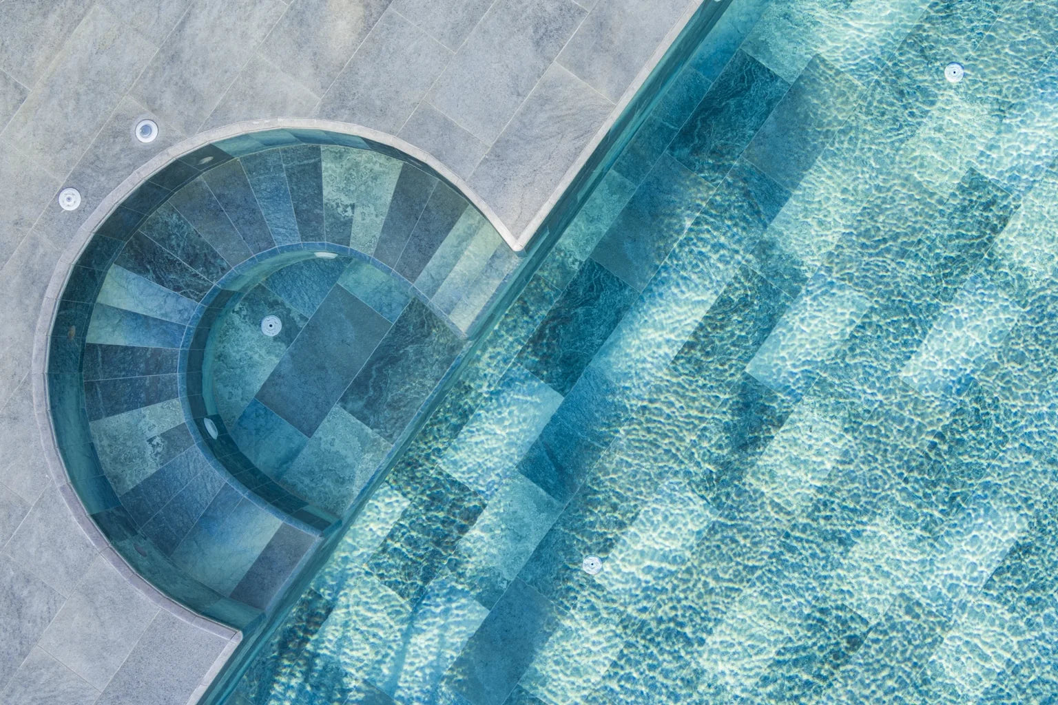 Relax pool & spa installation showing curved spa steps with blue-green porcelain pool tile and gray pool deck coping