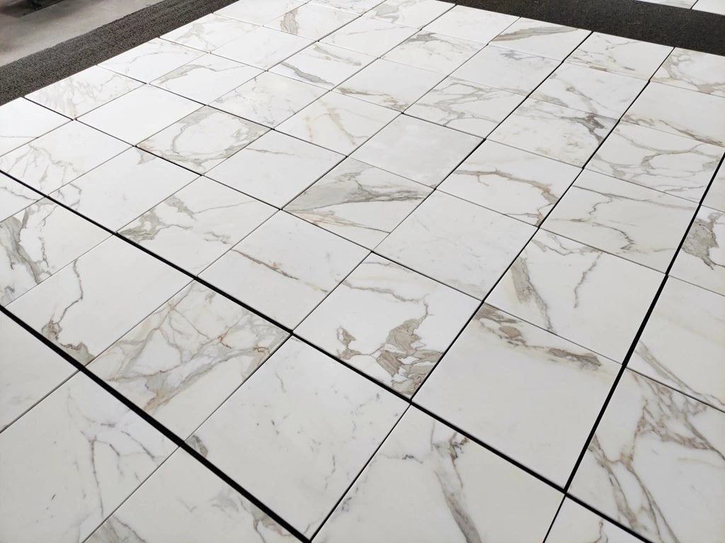 Calacatta Gold marble tile 18x18 honed, large lot layout showing white marble with soft gold and gray veining.