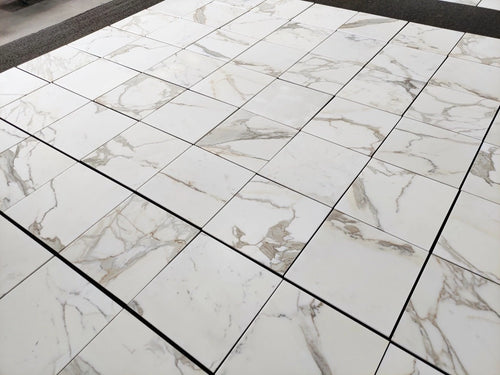 Calacatta Gold marble tile 18x18 honed, large lot layout showing white marble with soft gold and gray veining.