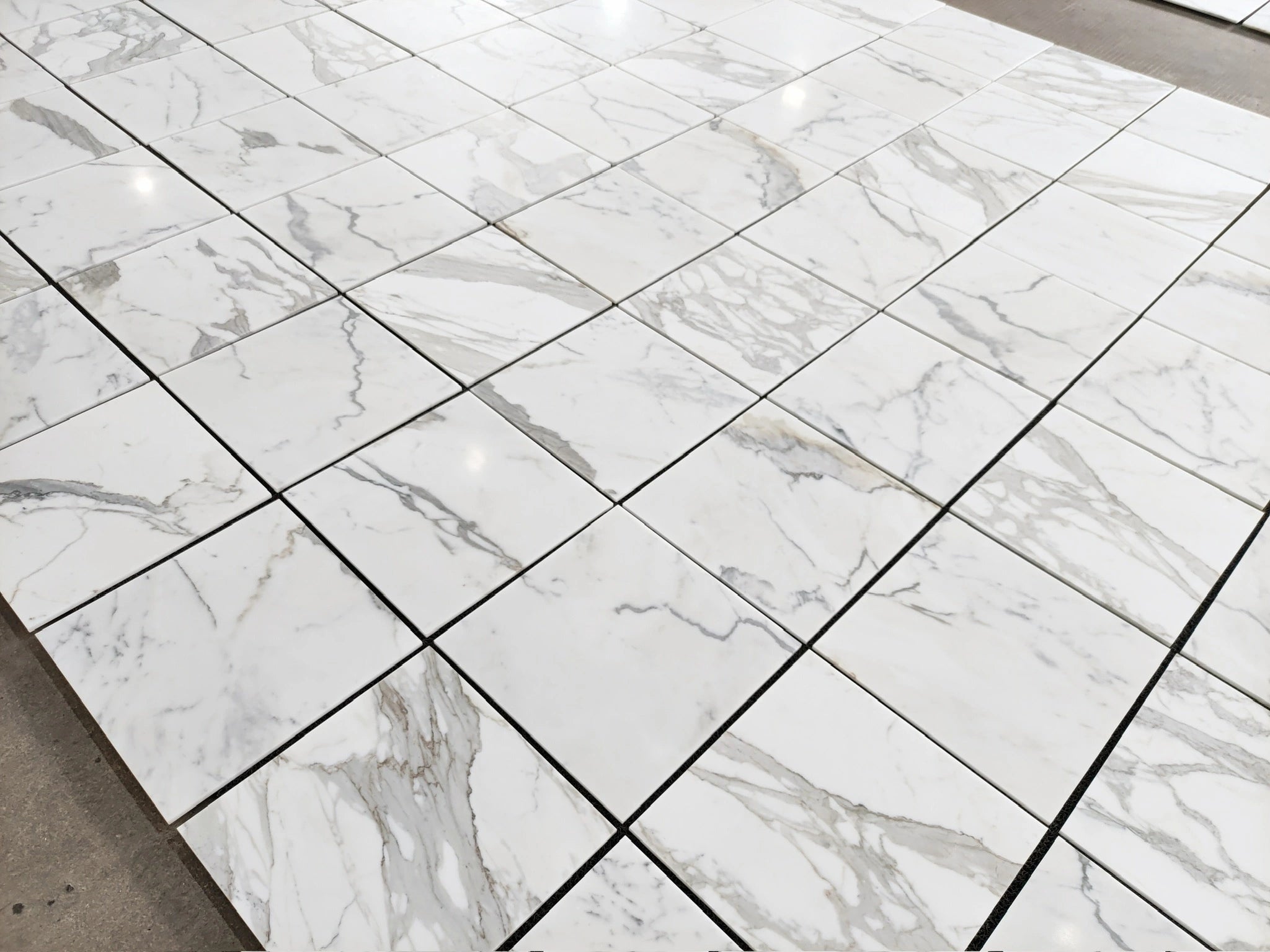 Calacatta Gold marble tile 18x18 honed, polished-look warehouse layout view showing mixed veining across multiple tiles.