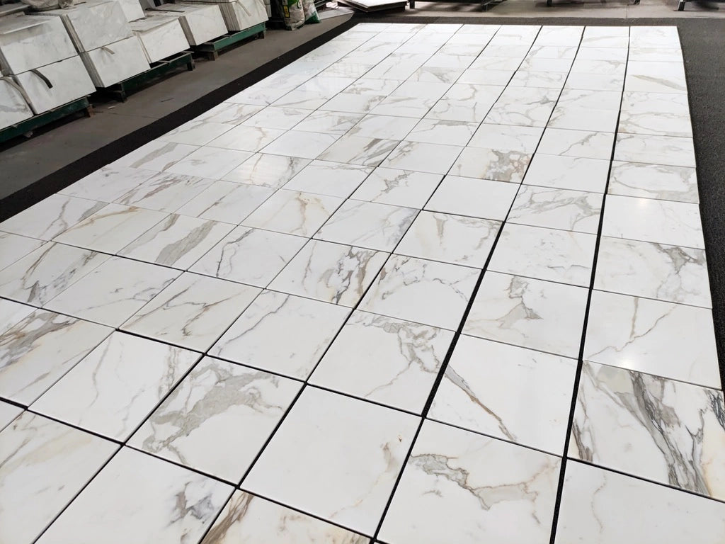 Calacatta Gold marble tile 18x18 honed, wide layout photo showing variation of gray and warm gold veining across the set.