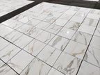 Calacatta Gold marble 18x18 polished tiles laid out in a grid, white background with gray and gold veining.