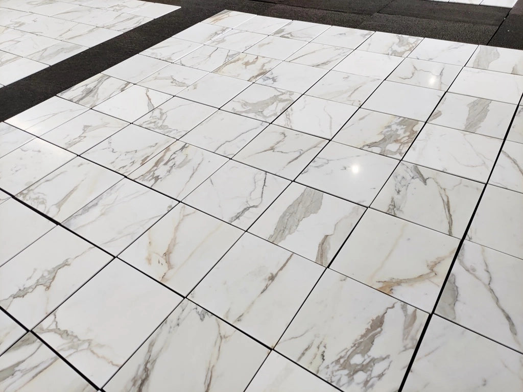 Calacatta Gold marble 18x18 polished tiles laid out in a grid, white background with gray and gold veining.