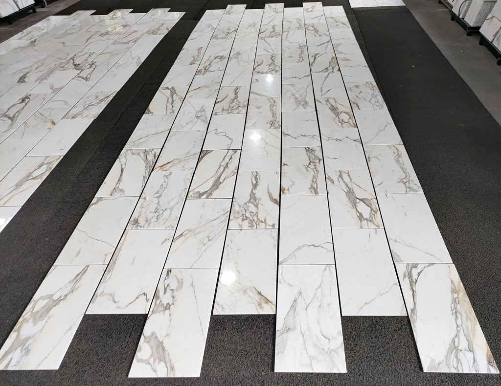 aria calacatta gold marble 12x24-patterned tiles arranged in a grid on a black floor.