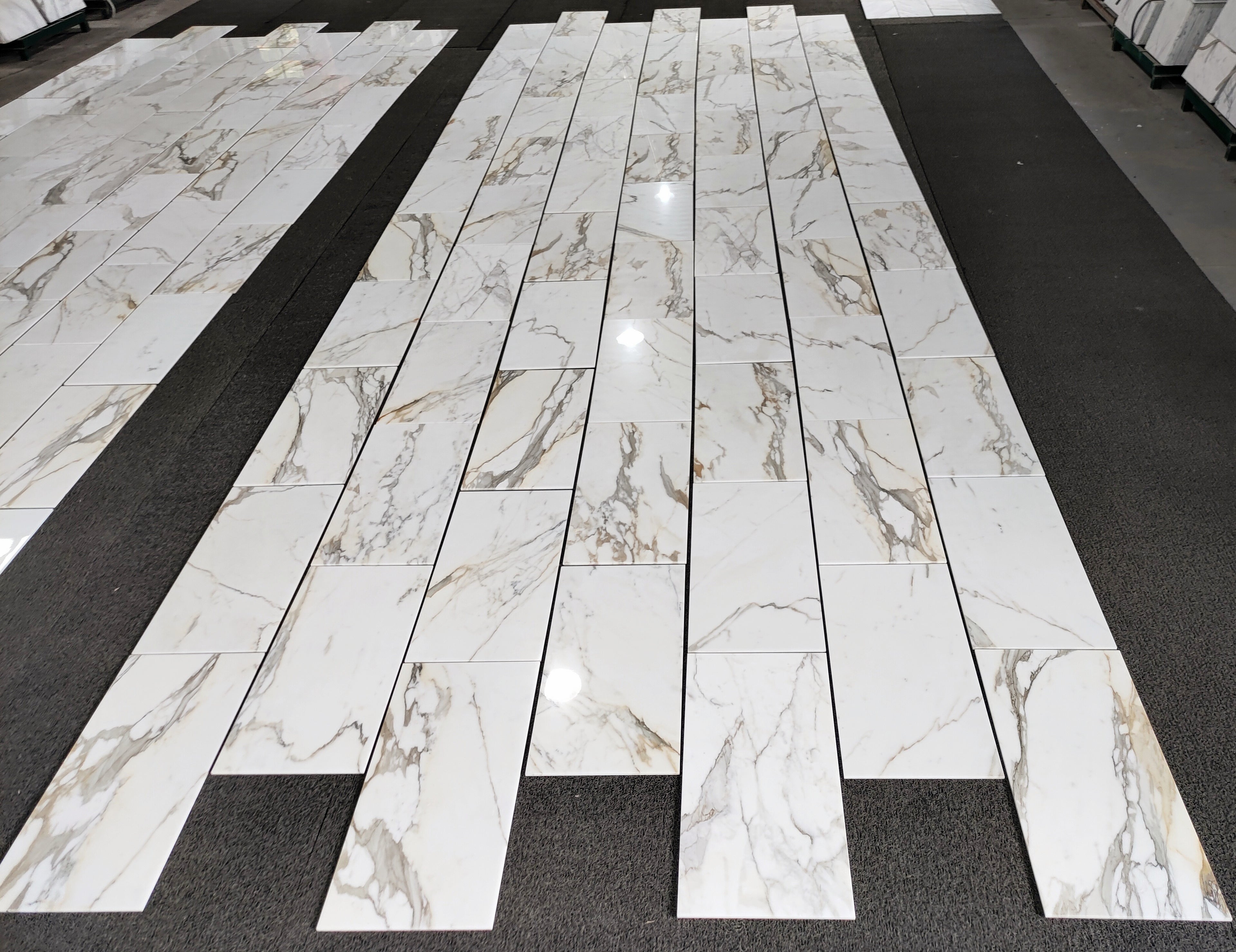 aria calacatta gold marble 12x24-patterned tiles arranged in a grid on a black floor.