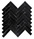 Aria Nero Marquina black marble 1x4 herringbone mosaic sheet, studio image showing deep black stone with bold white veining and natural high-contrast variation in a classic herringbone pattern.