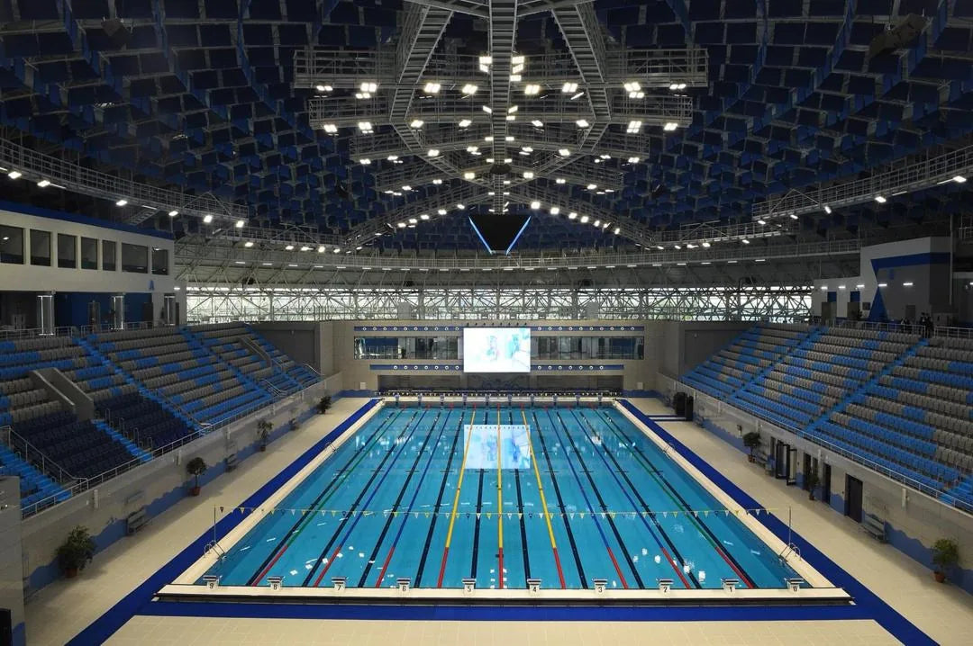 Olympic series indoor competition pool with stadium seating and lane lines.