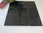 Black marble tiles on a white surface with a plant leaf in the corner.