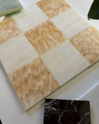 Checkered pattern of beige and white tiles on a white surface with a small black marble tile inset.