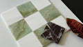 Checkered pattern of green and white tiles with a marbled brown tile on a white surface.