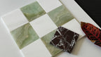 Checkered pattern of green and white tiles with a marbled brown tile on a white surface.